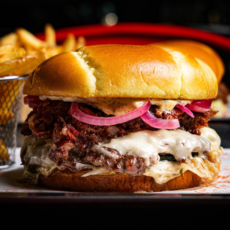 Signature burger sa topljenim sirom i ukiseljenim lukom, iza njega pomfrit